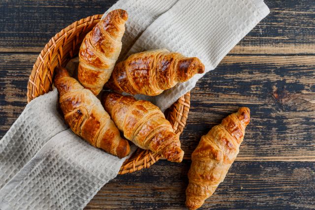 Croissant in basket with cloth on wooden table flat lay
